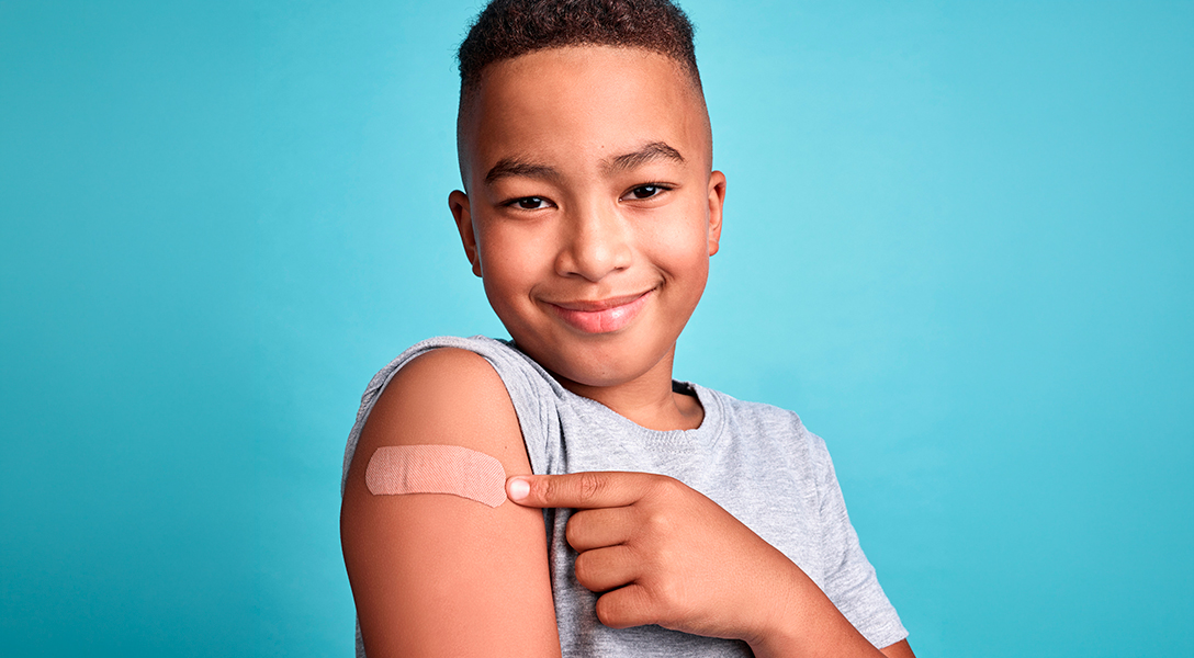 Adolescente sorrindo e apontando para o curativo no braço após receber a vacina contra o HPV