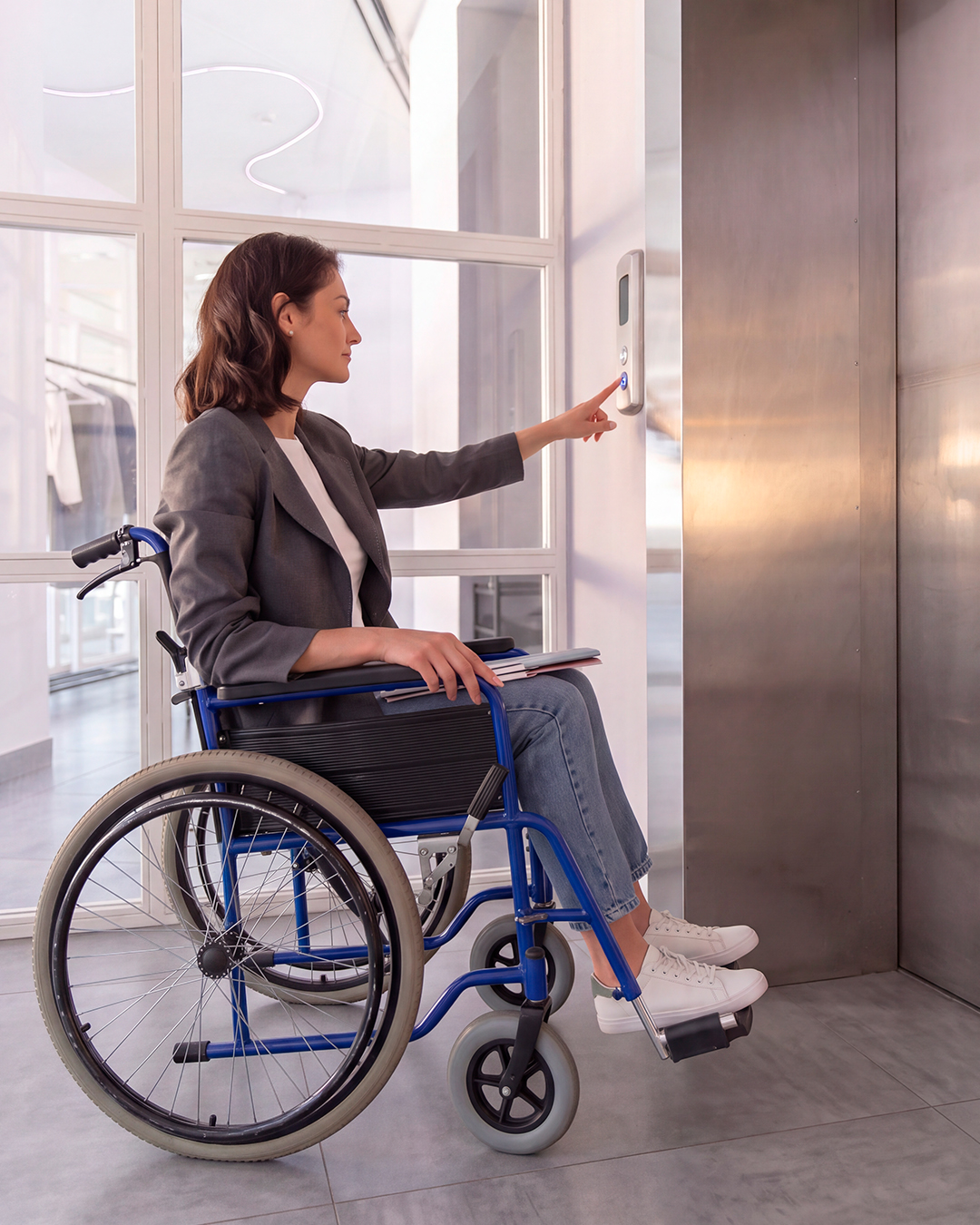 Mulher em cadeira de rodas acionando o botão do elevador