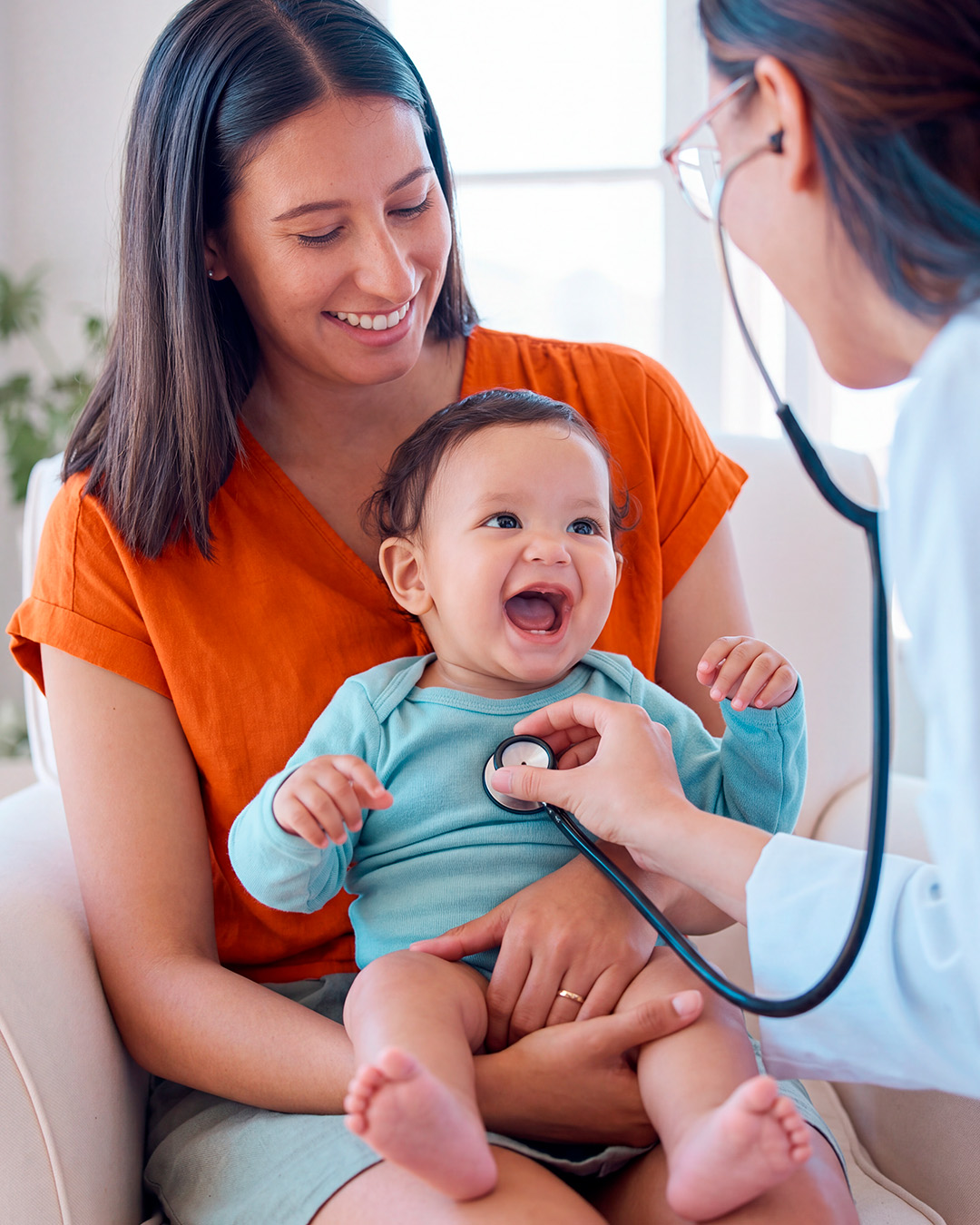 Pediatra examinando um bebê no colo da mãe durante o atendimento