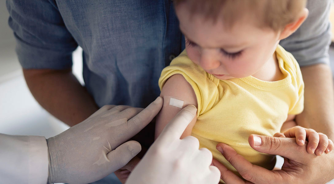 Bebê no colo recebendo curativo no braço após a vacina da gripe
