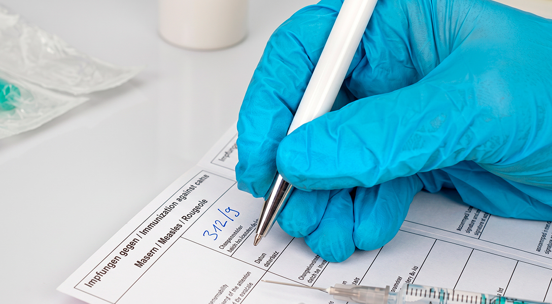 Mão com luva registrando a data de uma dose na caderneta de vacinação